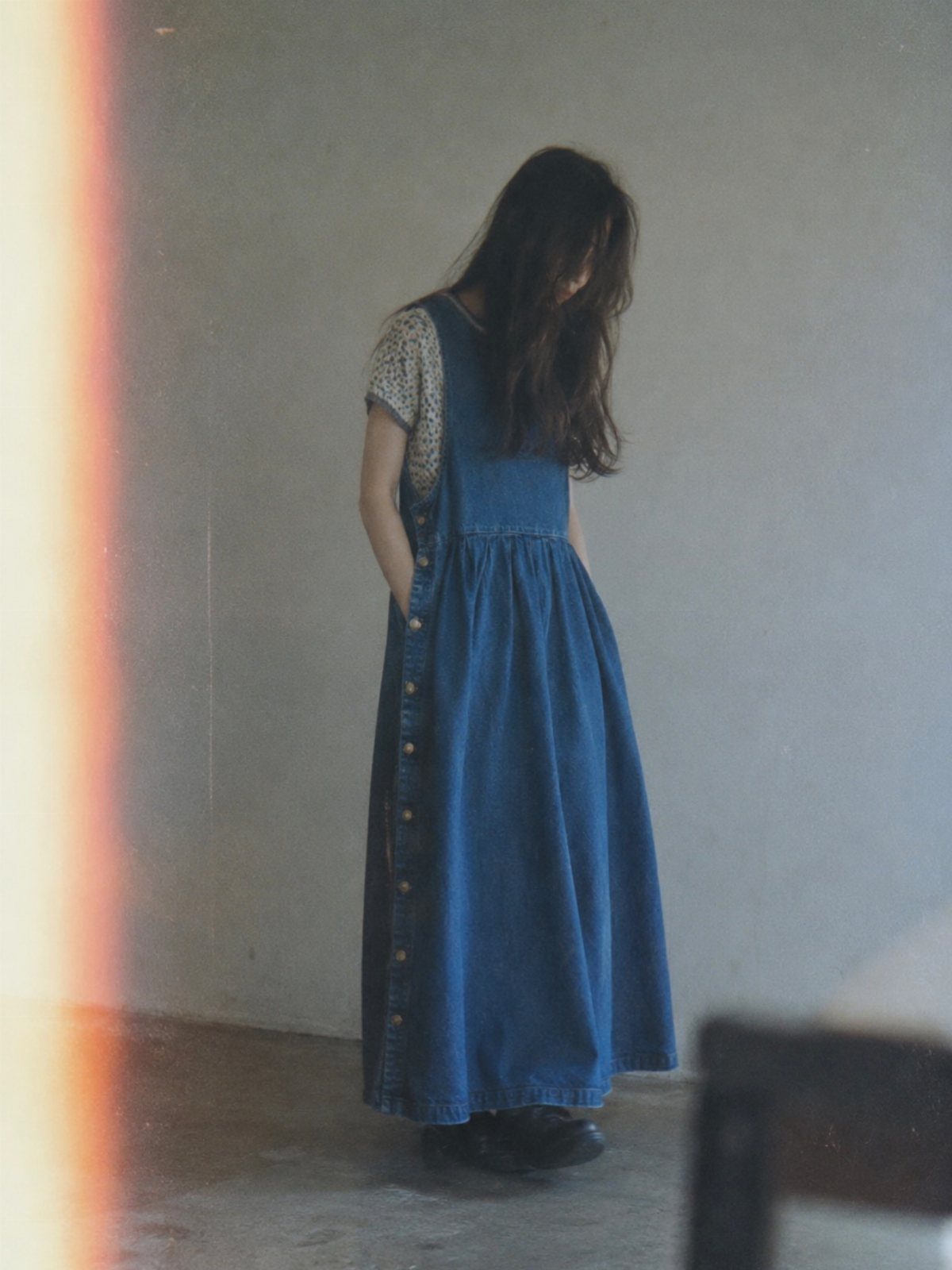 Woman wearing a long blue denim jumper dress over a patterned shirt.