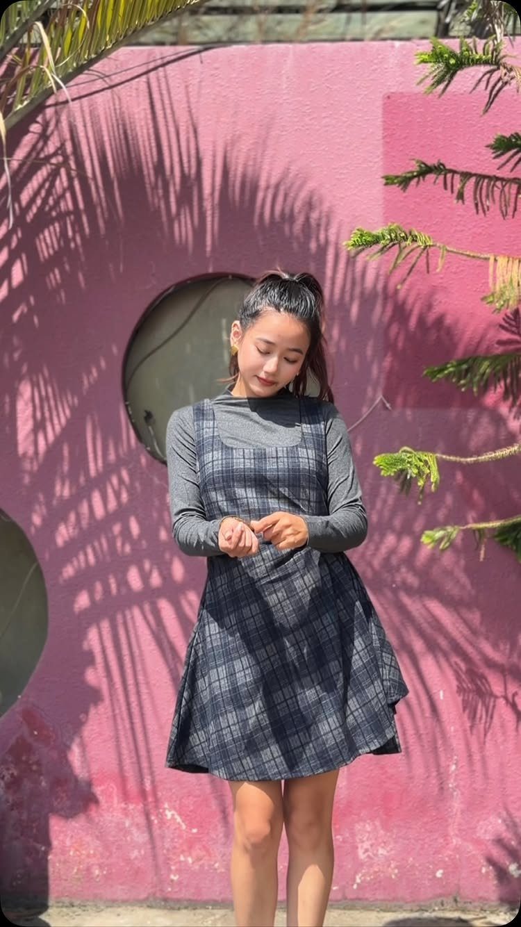 Woman wearing a grey plaid jumper dress over a grey turtleneck top.