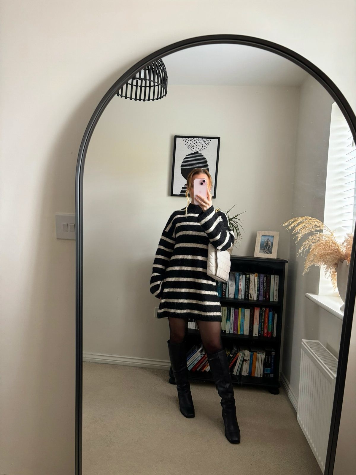 Woman in a black and white striped knit jumper dress and black boots.