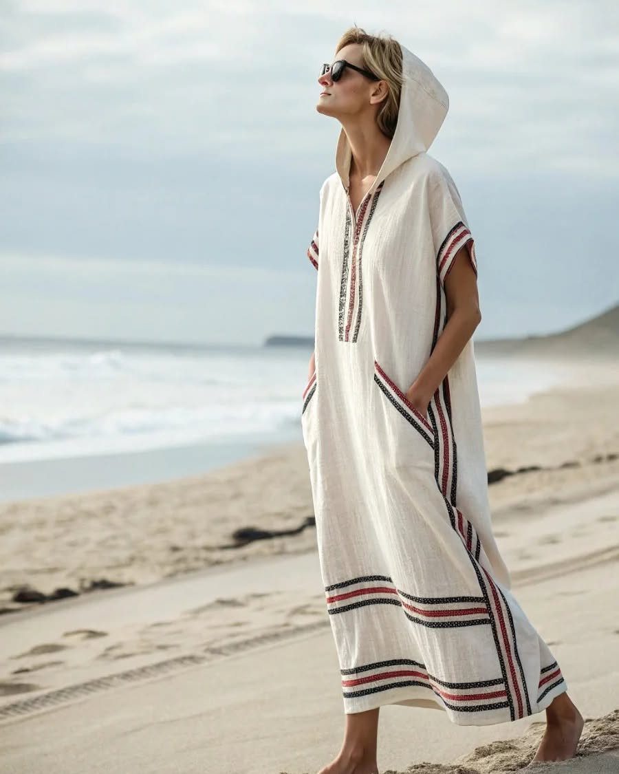 Woman in a white hooded linen beach dress with red and black stripes.
