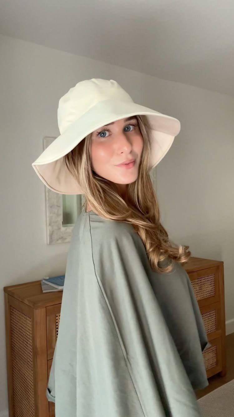 Woman wearing a wide-brimmed white sun hat and a sage green long-sleeved dress.