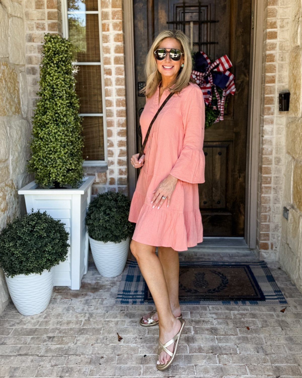 Woman in a peach lightweight summer dress with bell sleeves and gold sandals.