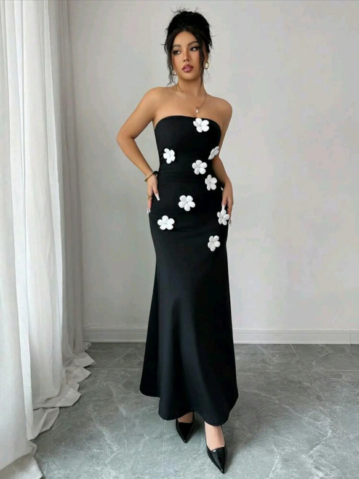 Woman in a strapless black maxidress with white 3D floral embroidery and black heels.