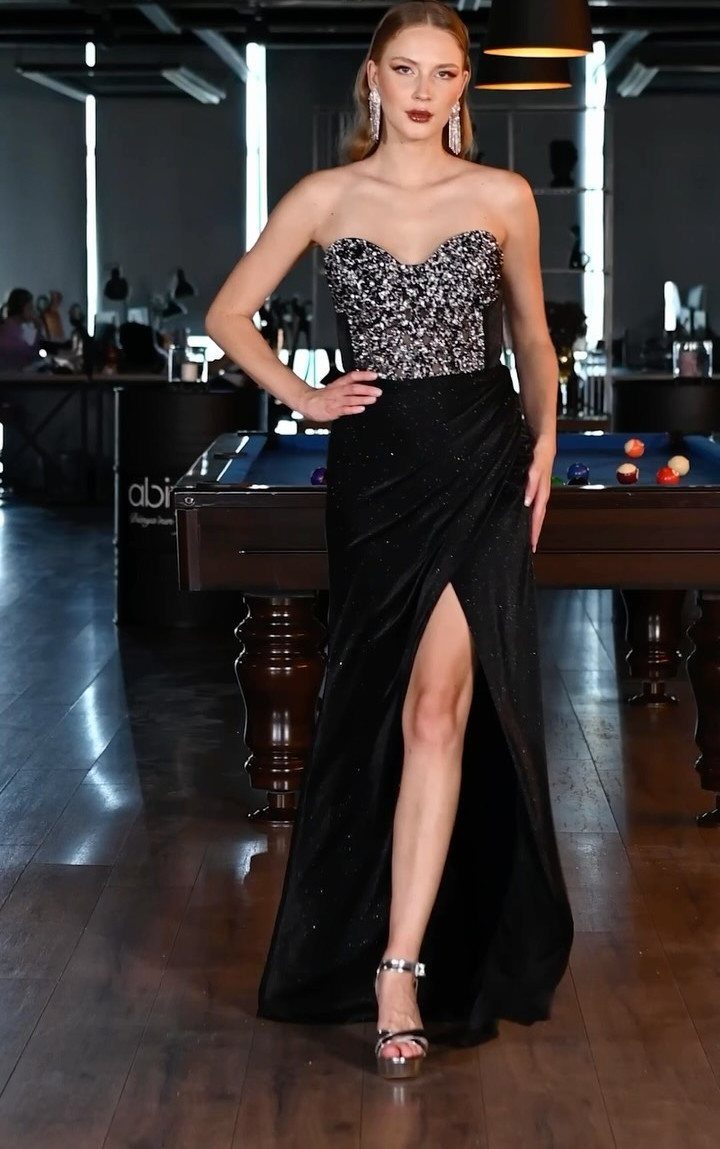 Woman in a black sequined strapless bustier maxidress posing by a pool table.