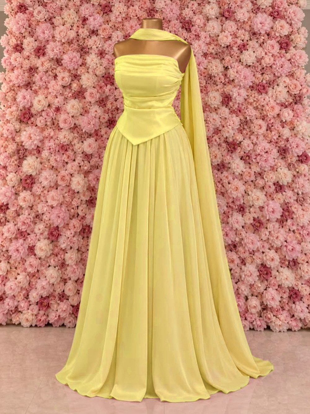 Yellow satin strapless maxidress on a mannequin against a pink flower wall