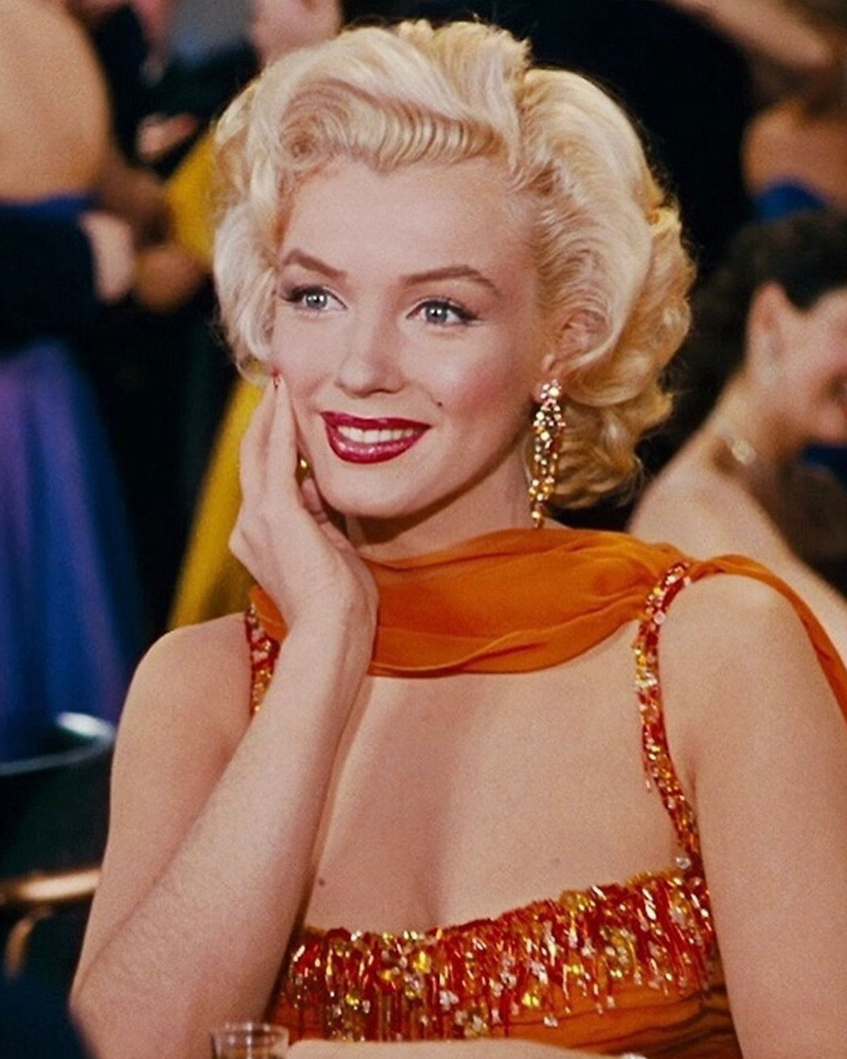 Marilyn Monroe wearing an orange sequined dress and matching neck wrap.