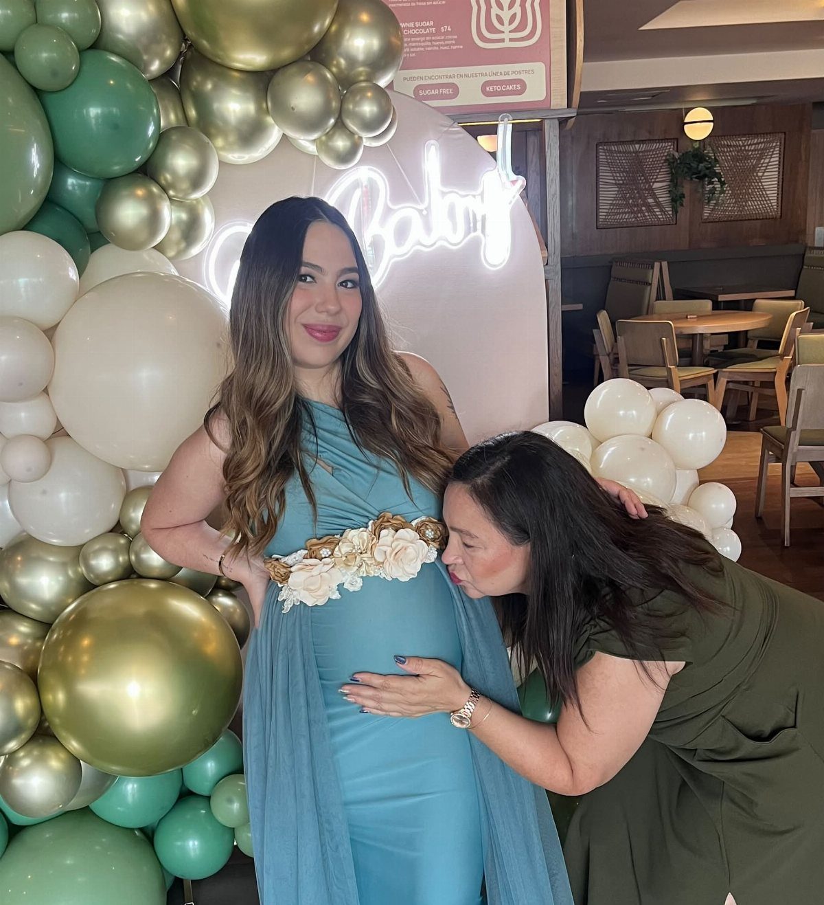 Pregnant woman wearing a blue maternity dress with a white flower sash.