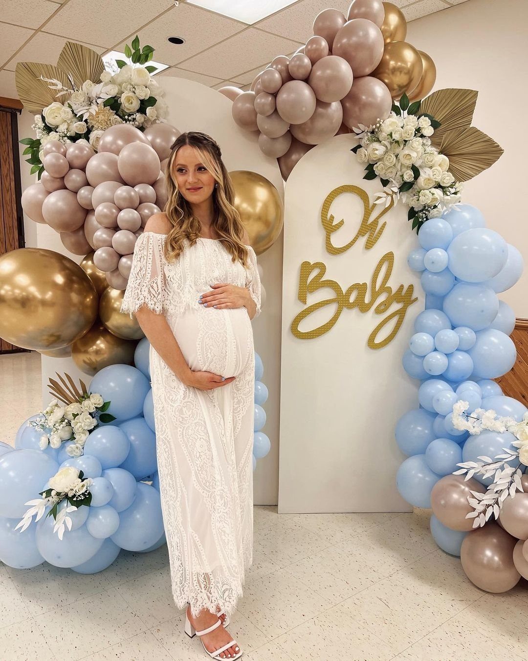 Pregnant woman in a white off-the-shoulder lace maxi dress at a baby shower.