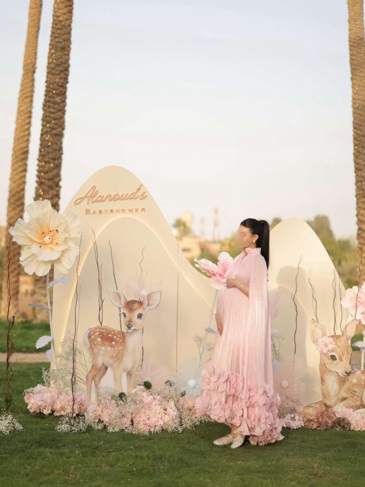 Pregnant woman in a ruffled pink maternity dress posing at a baby shower event.