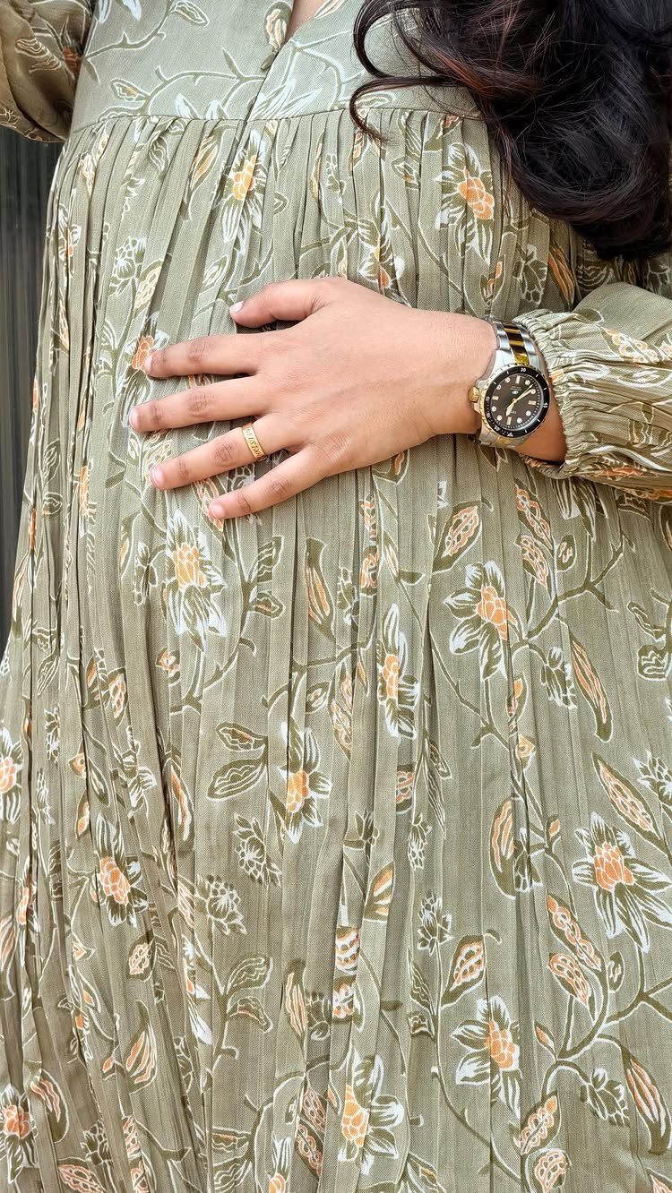 Pregnant woman in a sage green floral maternity dress with hand on bump