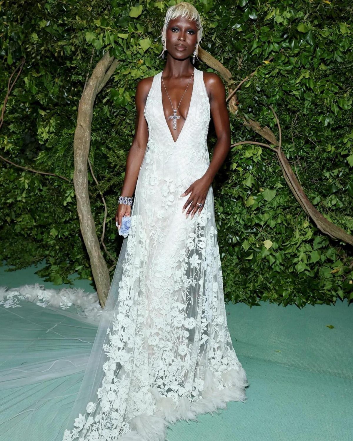 12 Met Gala Dresses That Defined Red Carpet Fashion 7 Woman in a white floral lace gown with a deep V-neckline standing outdoors.