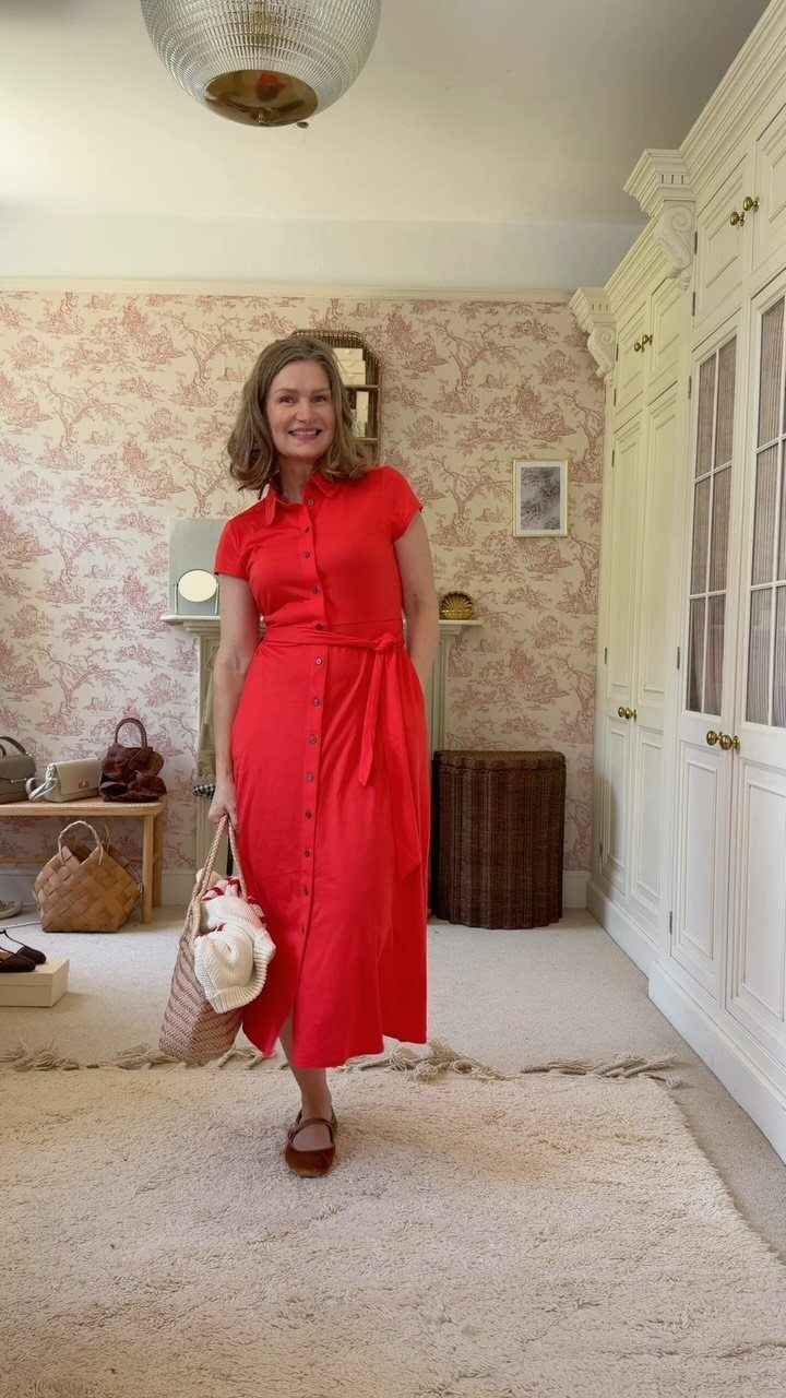 Woman wearing a red midi button-down dress standing in a room with floral wallpaper.