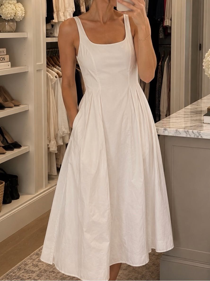 Woman wearing a white sleeveless poplin midi dress in a bright walk-in closet.