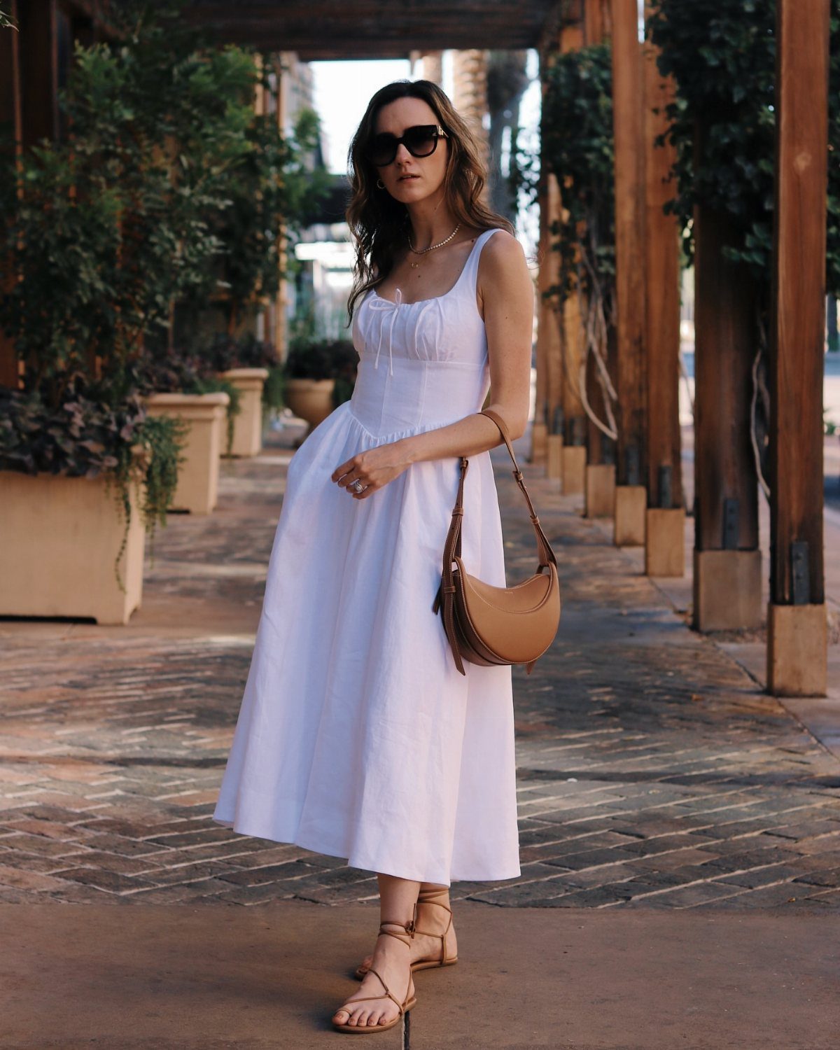 Woman in a white midi prairie dress with a brown bag on brick walkway
