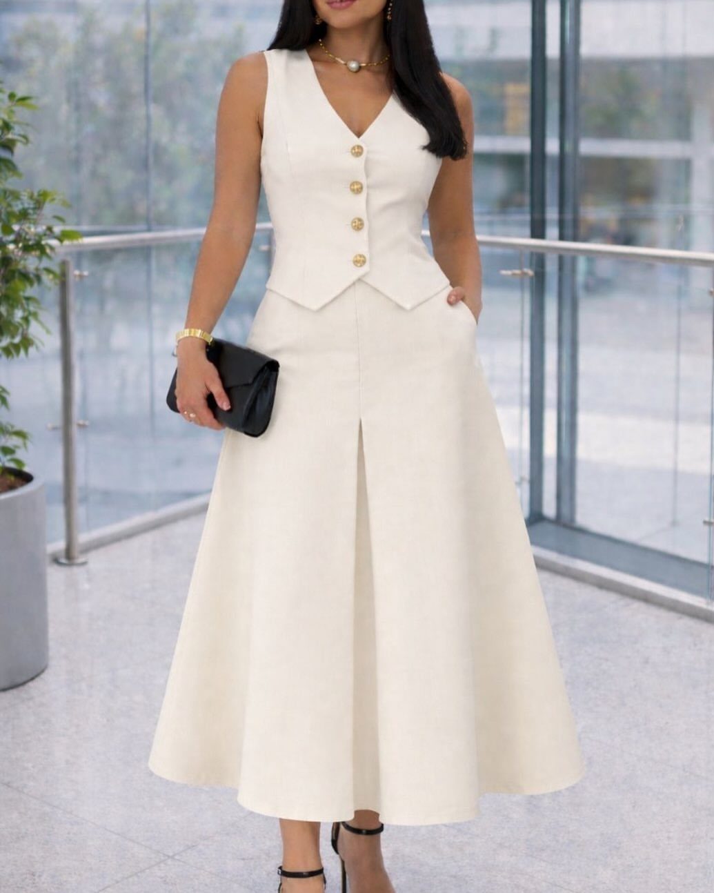 Woman in a white sleeveless midi dress with a buttoned vest bodice and flared skirt.