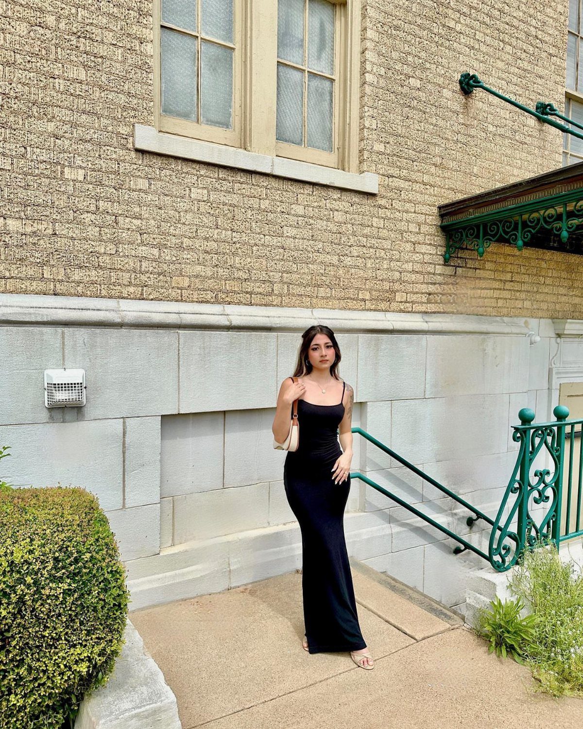 Petite Maxi Dresses in 10 Styles for Every Occasion 2 Woman in a form-fitting black maxi dress standing by a stone building.