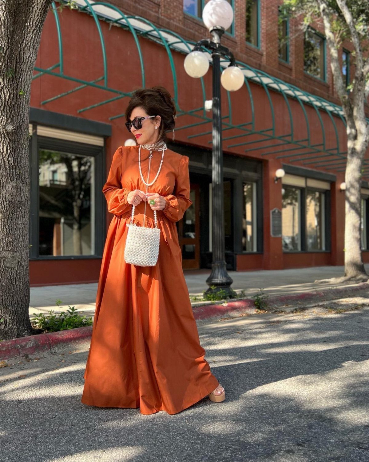 Petite Maxi Dresses in 10 Styles for Every Occasion 5 Woman in a burnt orange long-sleeved maxi dress standing on a sunny sidewalk.