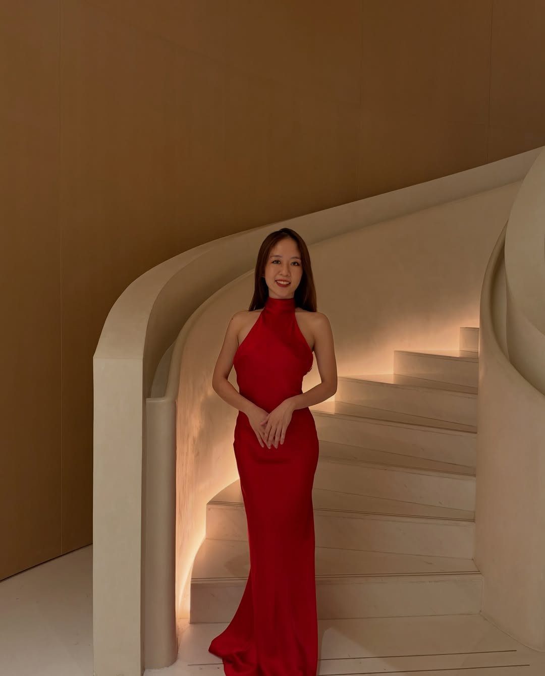 Petite Maxi Dresses in 10 Styles for Every Occasion 3 Woman in a red halter-neck maxi dress posing on a white curved staircase.