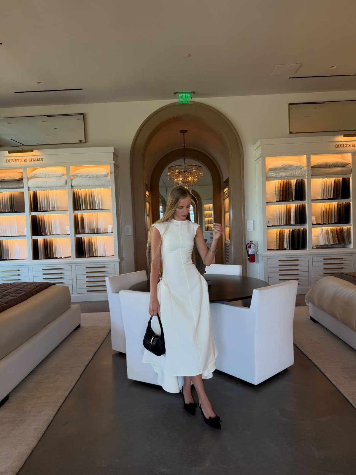 Petite Maxi Dresses in 10 Styles for Every Occasion 7 Woman in a sleeveless white maxi dress and black heels in a showroom.