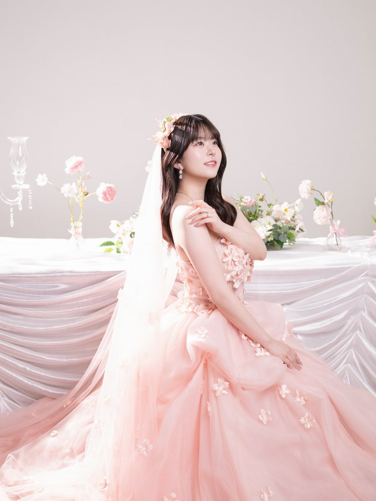 Woman in a pink floral ballgown and white veil posing in a studio