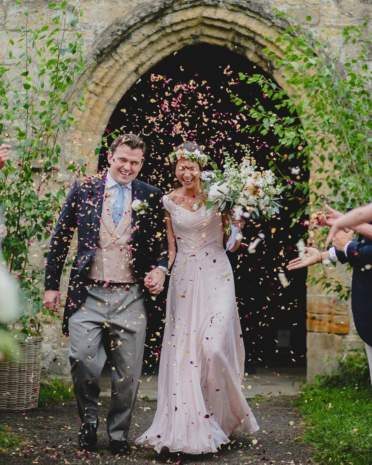 Bride in blush pink gown and groom walking through confetti at wedding