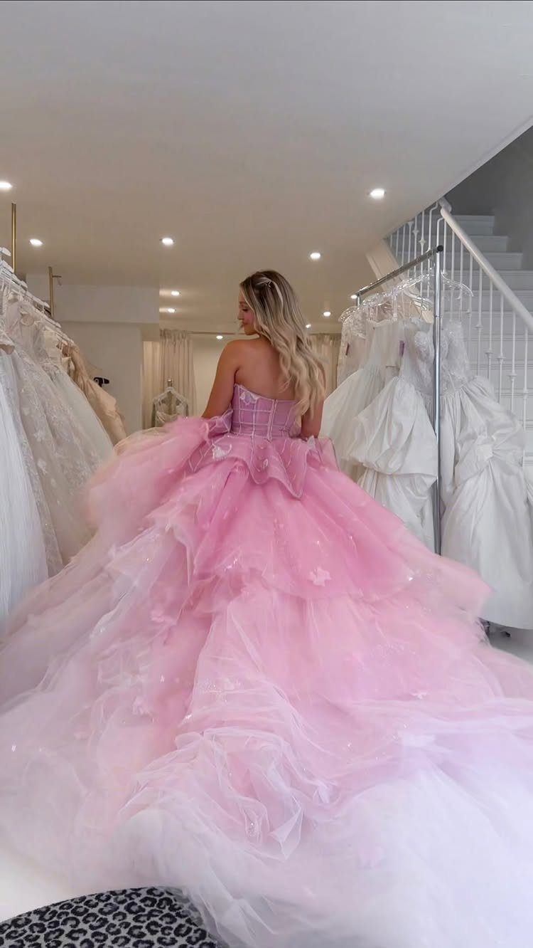 Woman wearing a voluminous tiered pink wedding dress in a bridal boutique.