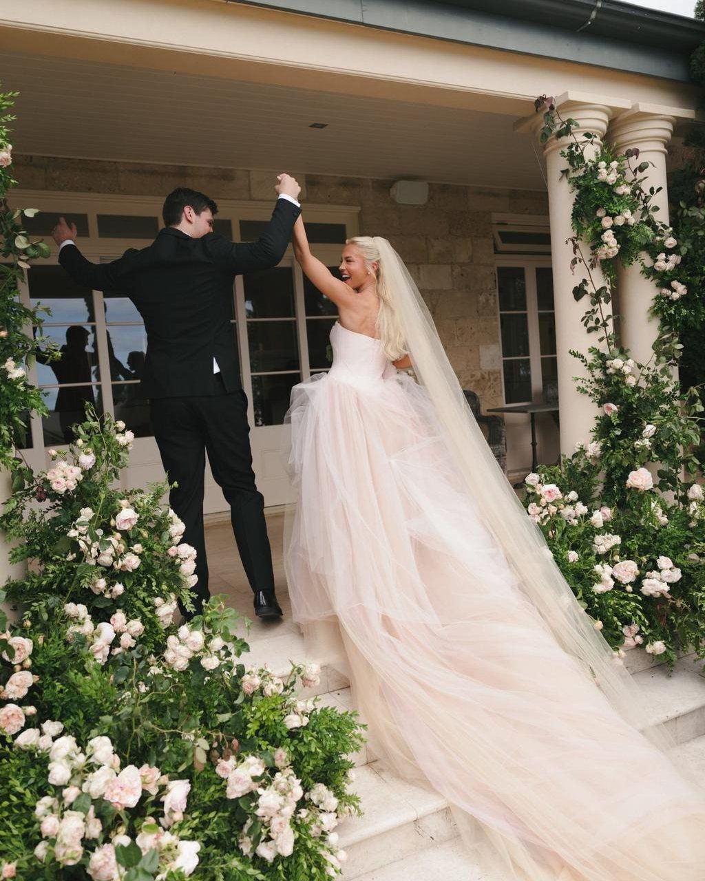 Bride in a strapless blush pink tulle gown and groom in a black tuxedo.