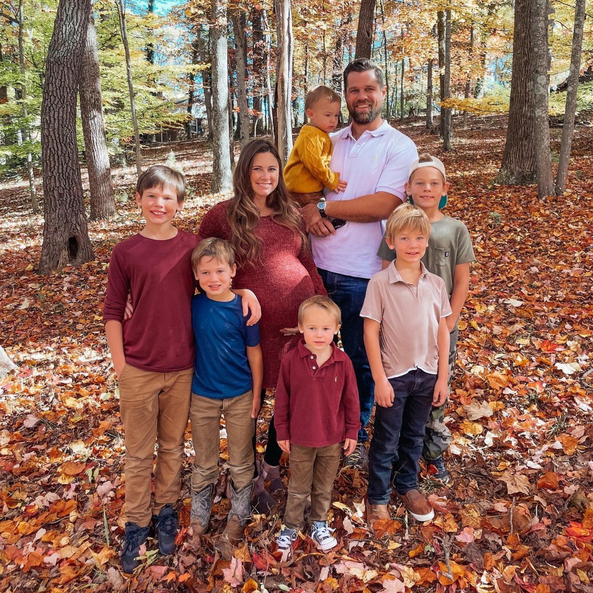 Pregnant woman and family wearing coordinating autumn colors posing in a fall forest.