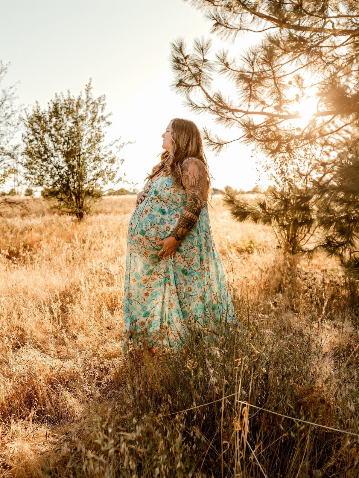 Pregnant woman in a light blue floral maxi dress standing in a sunny field