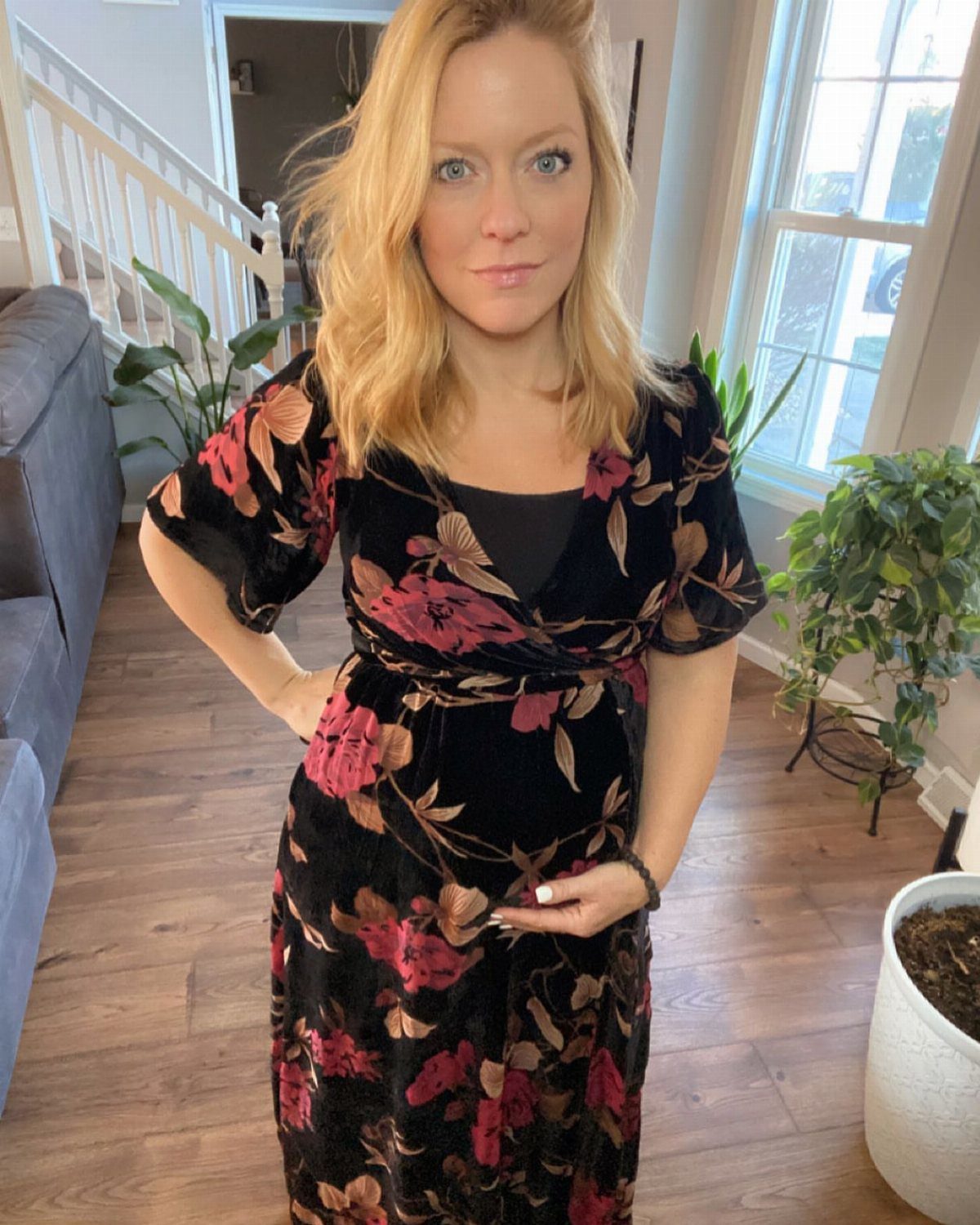 Pregnant woman wearing a black velvet wrap dress with red floral patterns indoors.