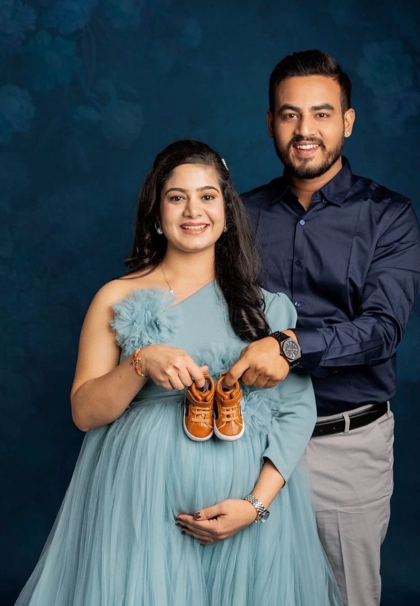 Pregnant woman in blue tulle gown and man holding baby shoes.