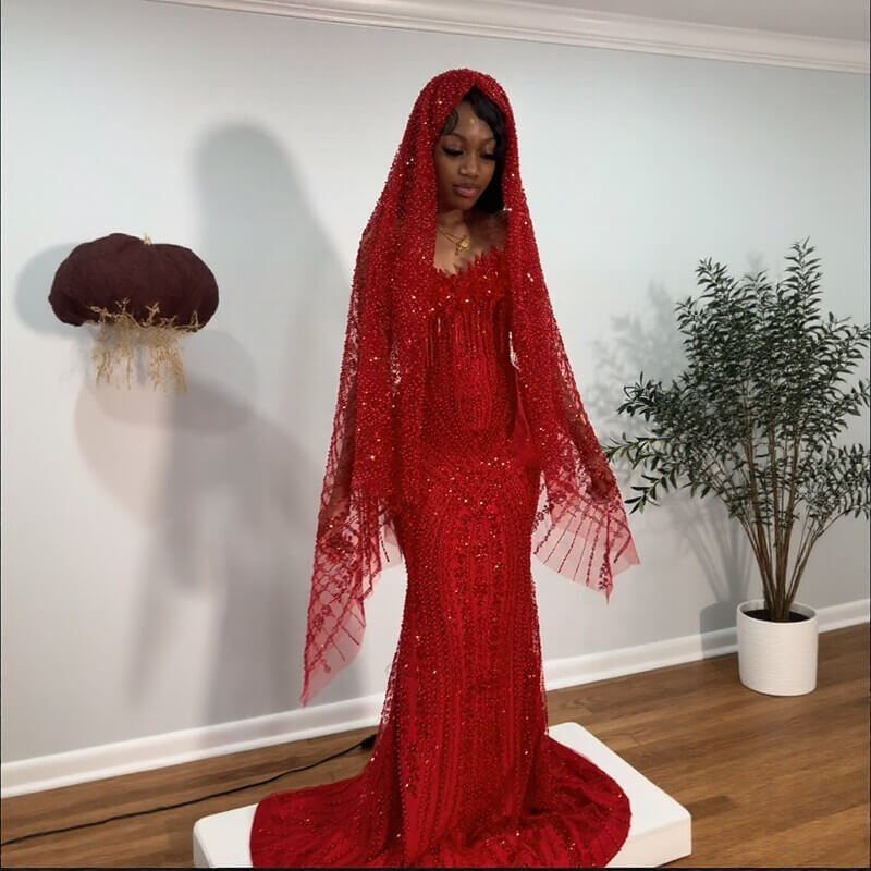 Woman in a red sequined mermaid gown and matching hooded cape standing indoors.