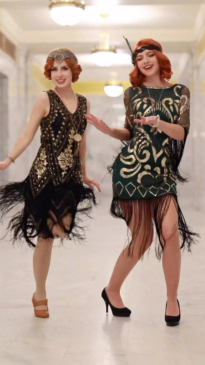 Two women wearing gold beaded drop-waist flapper dresses with long fringe and headbands.