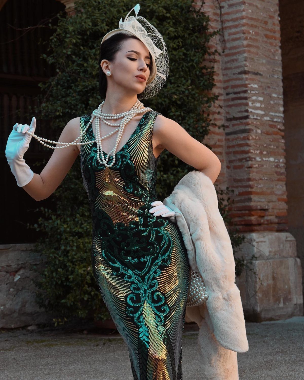 Woman in a green sequined 1920s dress with pearls and a feathered headpiece.