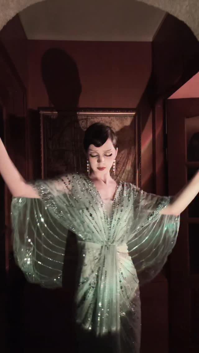 Woman in a shimmering green sequined 1920s flapper dress posing in a dark room.