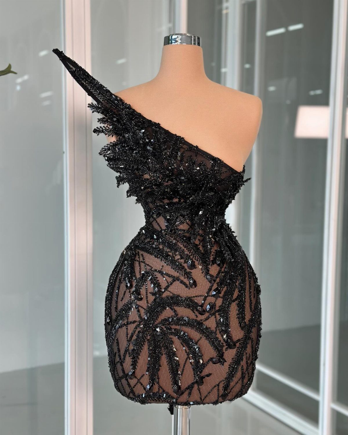 One-shoulder short black dress with intricate beading and a wing-like shoulder on mannequin.