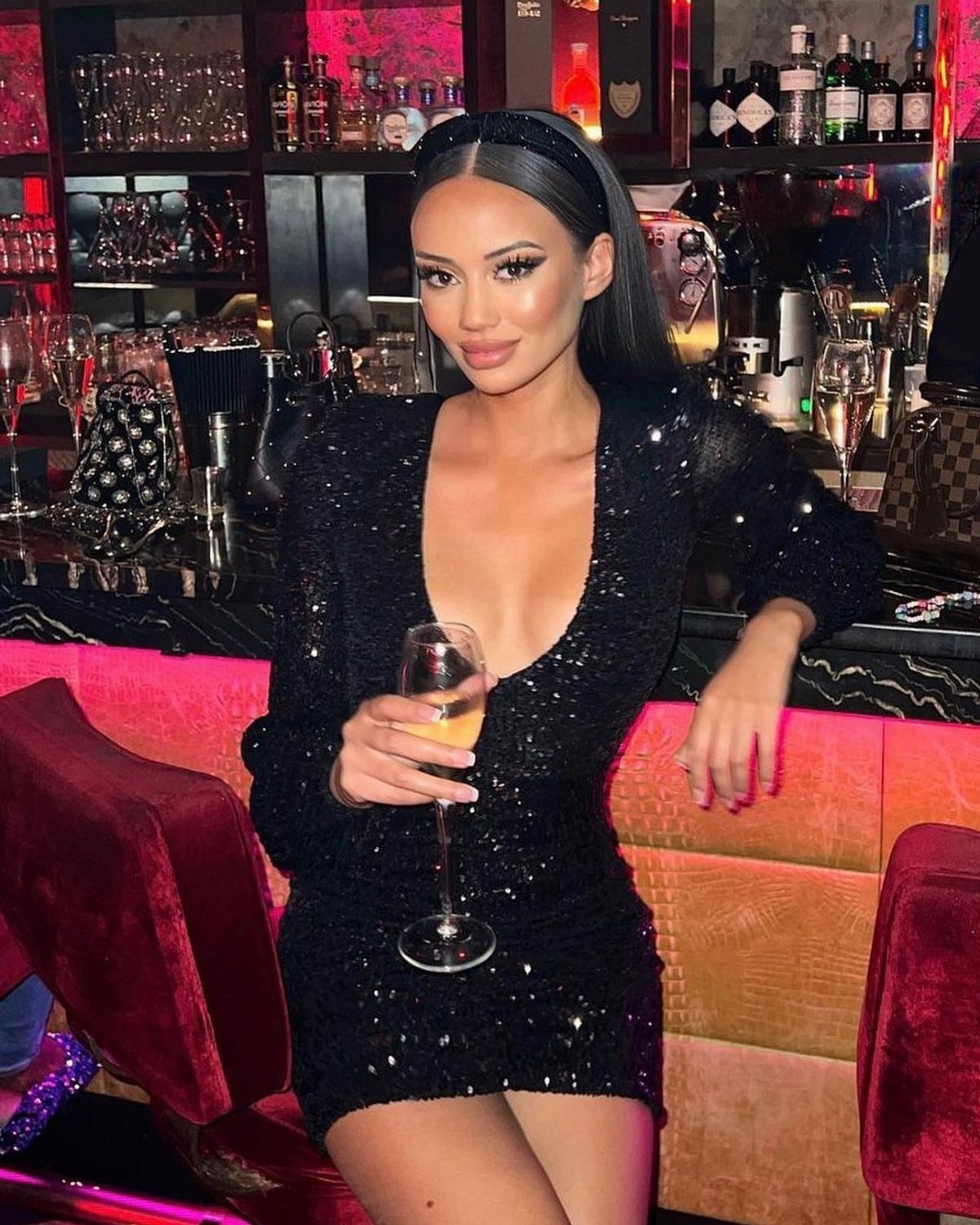 Woman in a short sparkling black sequined dress holding a champagne glass in a bar
