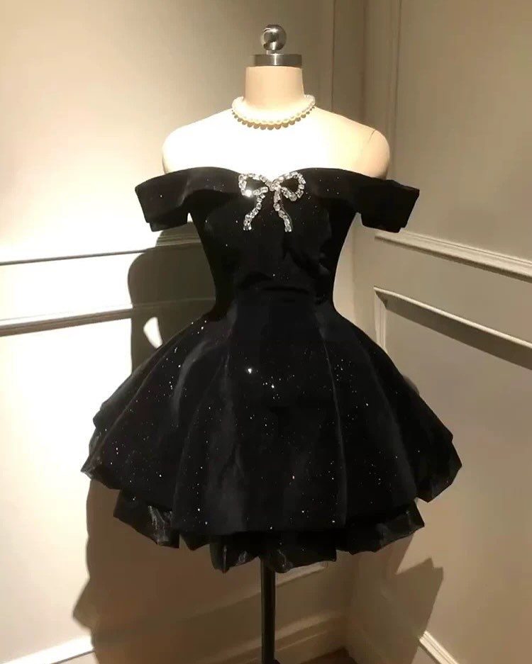 Short black off-the-shoulder dress with a silver bow on a white mannequin.