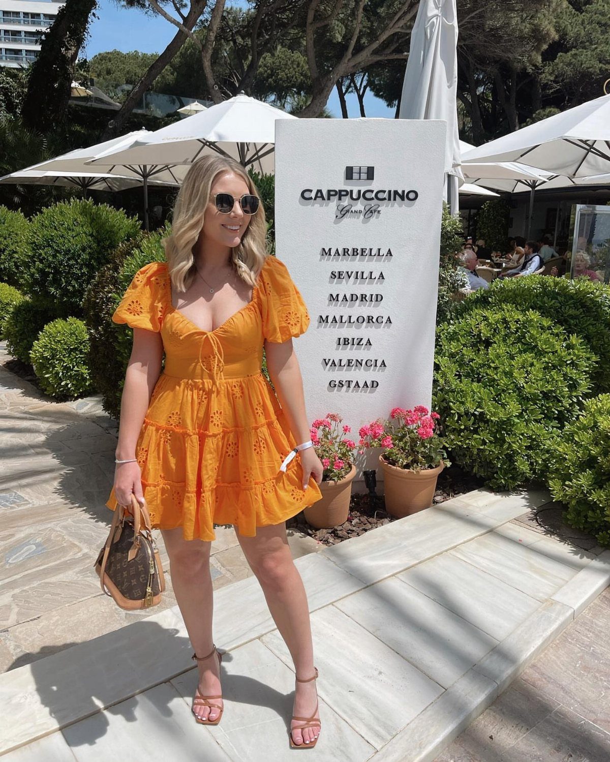 8 Short Summer Dresses Zara Shoppers Love Right Now 8 Woman in orange eyelet mini dress standing by a white sign outdoors.