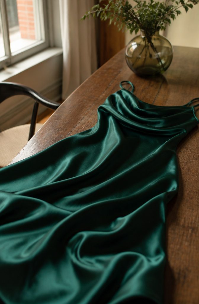 Silk Cocktail Dresses: Styles That Move From Day to Evening 1 Close-up of a silk cocktail dress in deep emerald color on a textured surface.