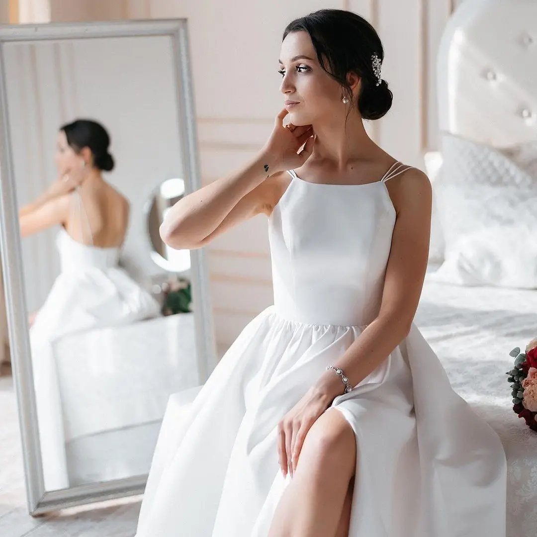 Simplistic Wedding Dress Ideas: 6 Elegant Styles to Consider 1 Woman in a plain white minimalist wedding dress sitting on a bed by a mirror