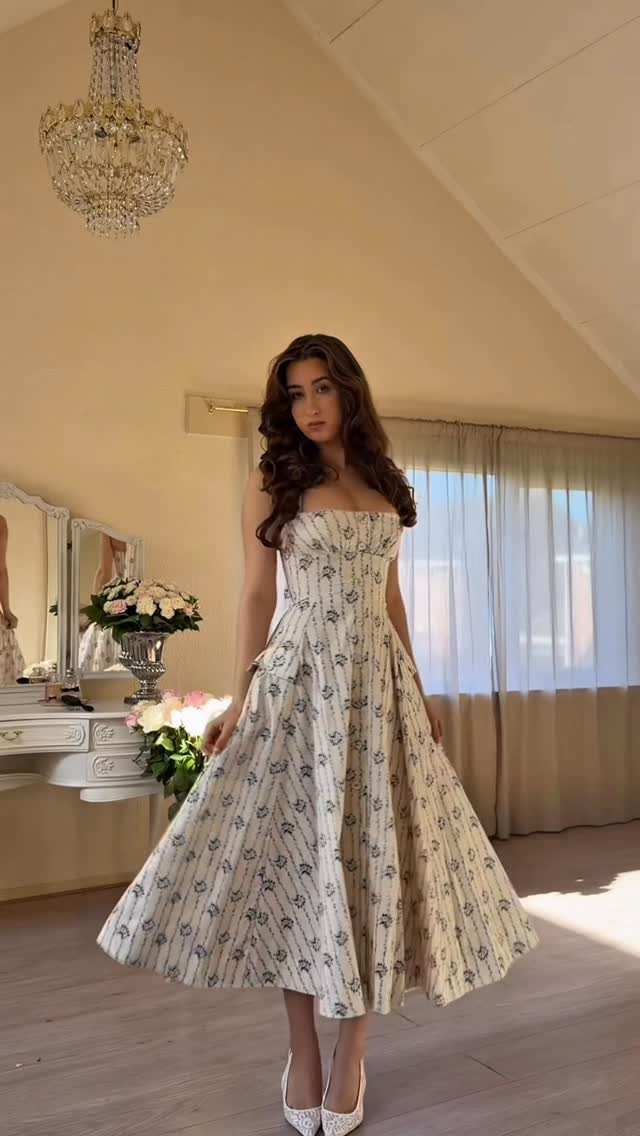 6 Spring Break Dresses to Pack for Your Next Getaway 3 Woman in a strapless cream floral midi dress and white heels in a bright room.