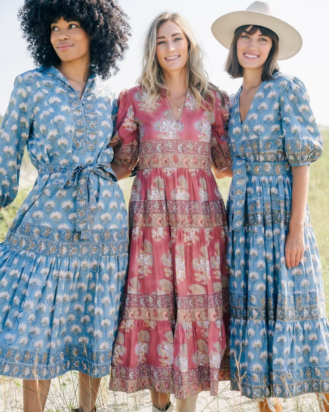 6 Spring Break Dresses to Pack for Your Next Getaway 1 Three women wearing colorful, flowy patterned maxi dresses standing in a sunny field.