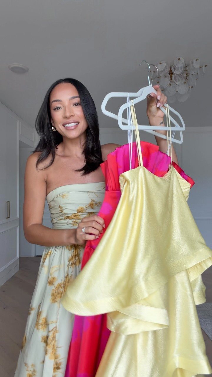 Woman wearing a cream floral strapless dress while holding pink and yellow dresses.