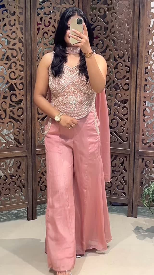 Woman wearing a pink beaded top and matching wide-leg trousers in front of wood carving.