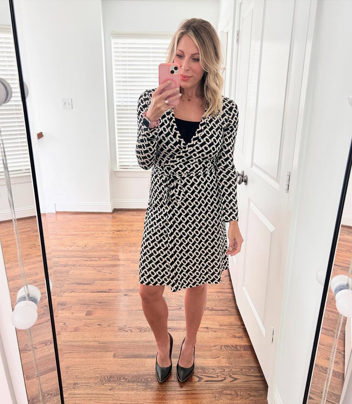 9 Stylish Work Dresses That Keep You Polished All Day 1 Woman wearing a black and white patterned wrap dress and black pointed heels.