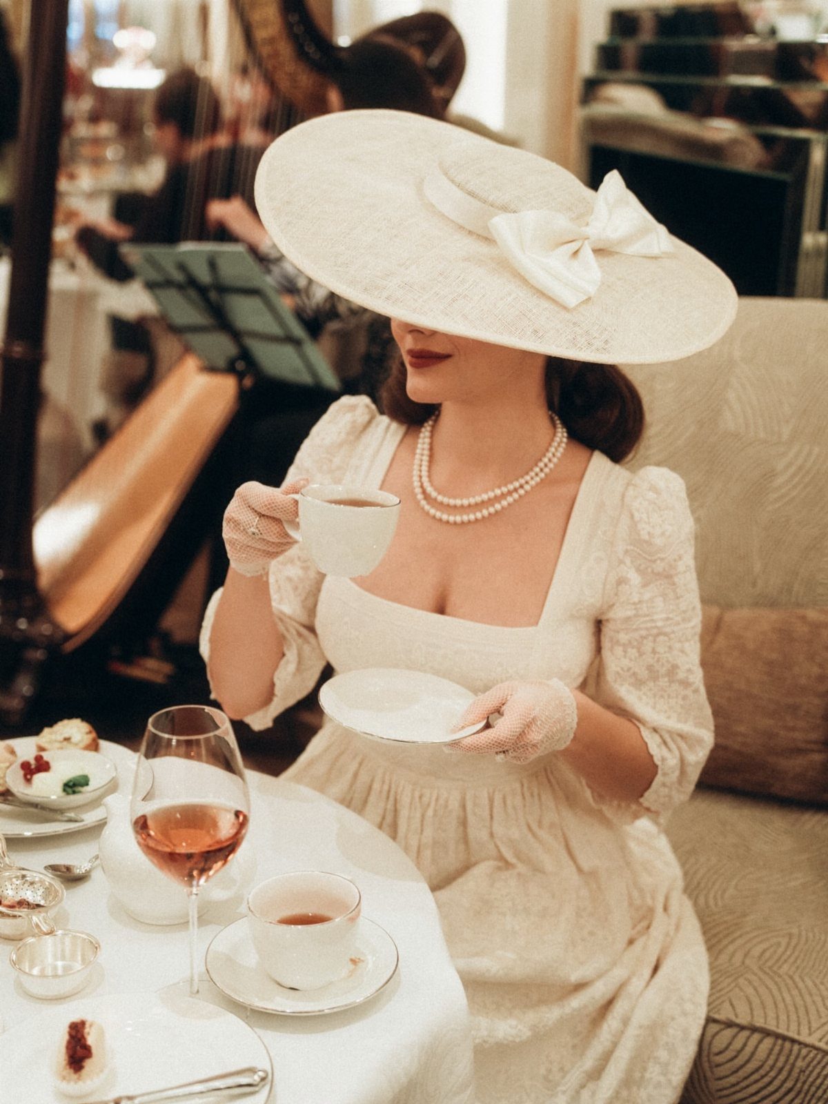 Woman in a white lace dress wearing a wide-brimmed white hat and pearls.