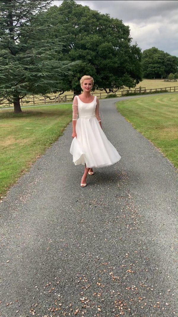 Woman in a white tea-length dress standing on a gravel path near trees