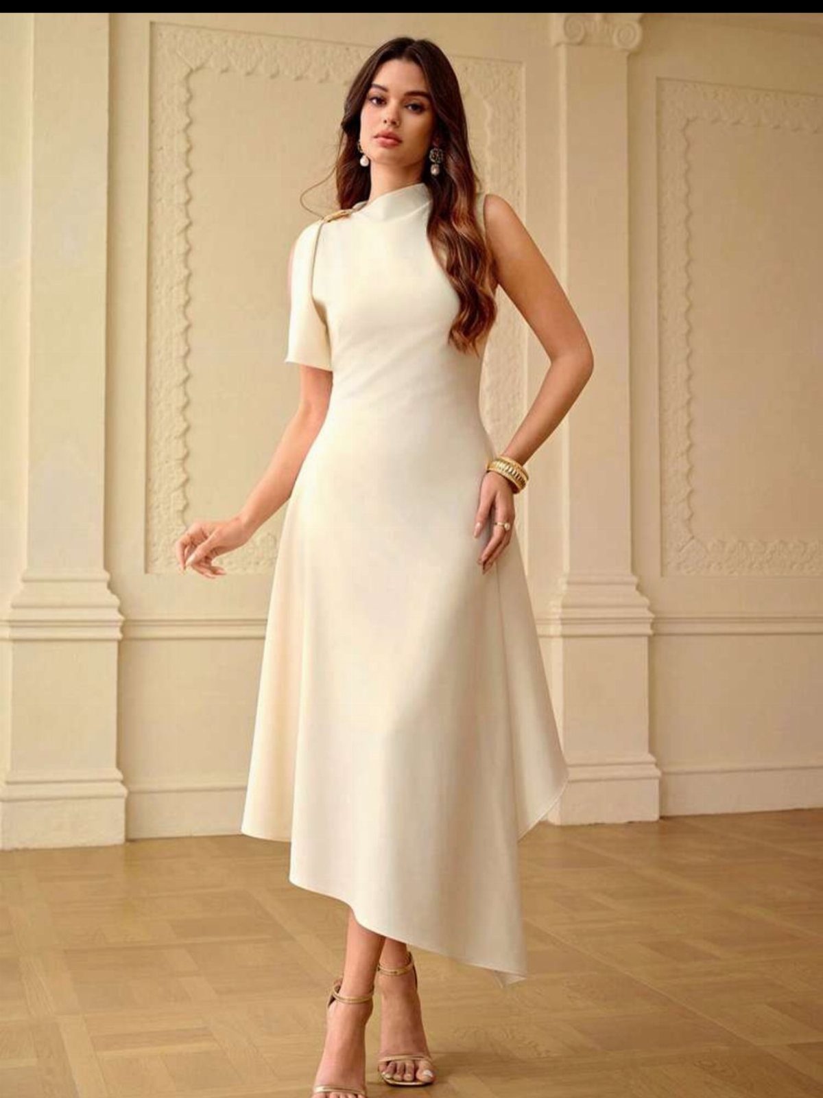 Woman wearing a cream asymmetrical dress with an uneven hemline in a bright room.