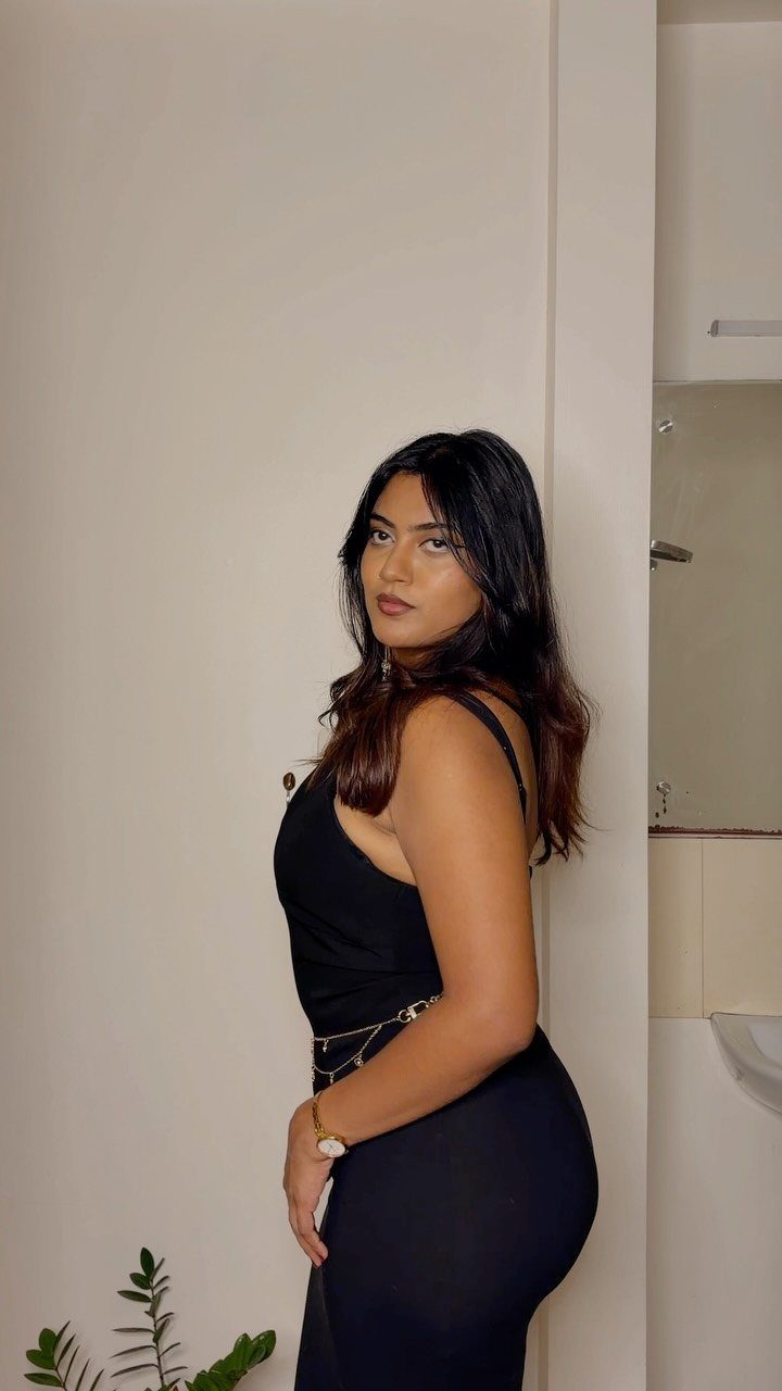Woman wearing a form-fitting black bodycon dress with a gold chain belt.